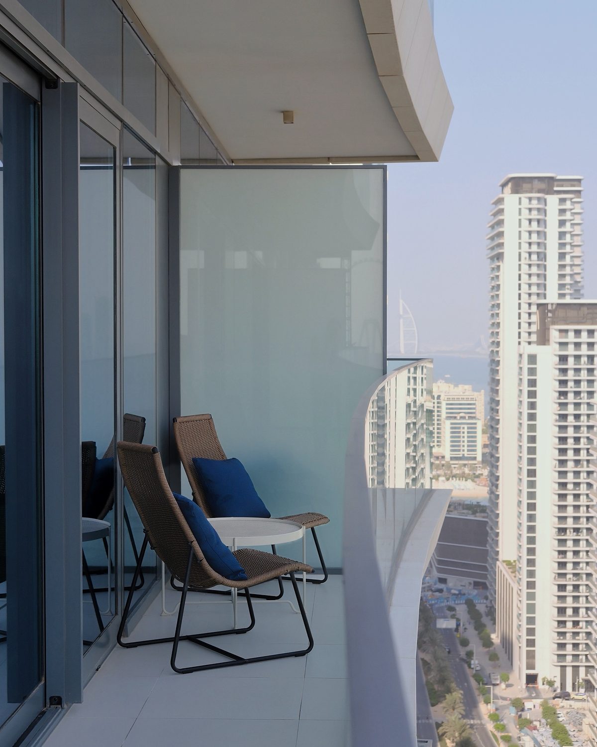 Balcony of the Dubai Harbour apartment with two rattan chairs, blue cushions and the Dubai Marina skyline