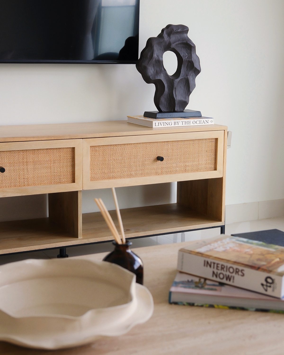 Rattan TV console with a black sculpture and books, ceramic bowl on the coffee table in front