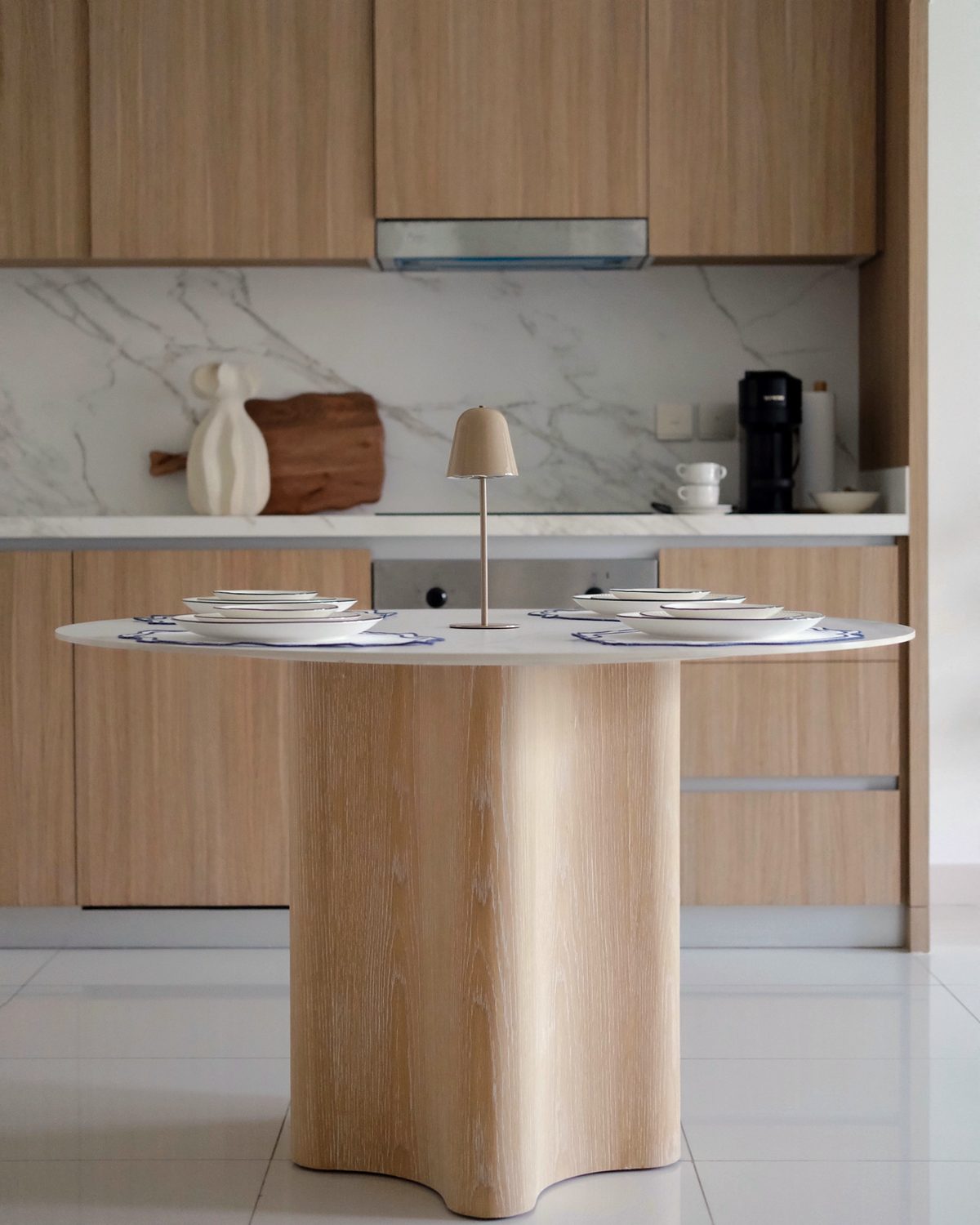 Round dining table on a sculpted oak base, with the oak kitchen behind