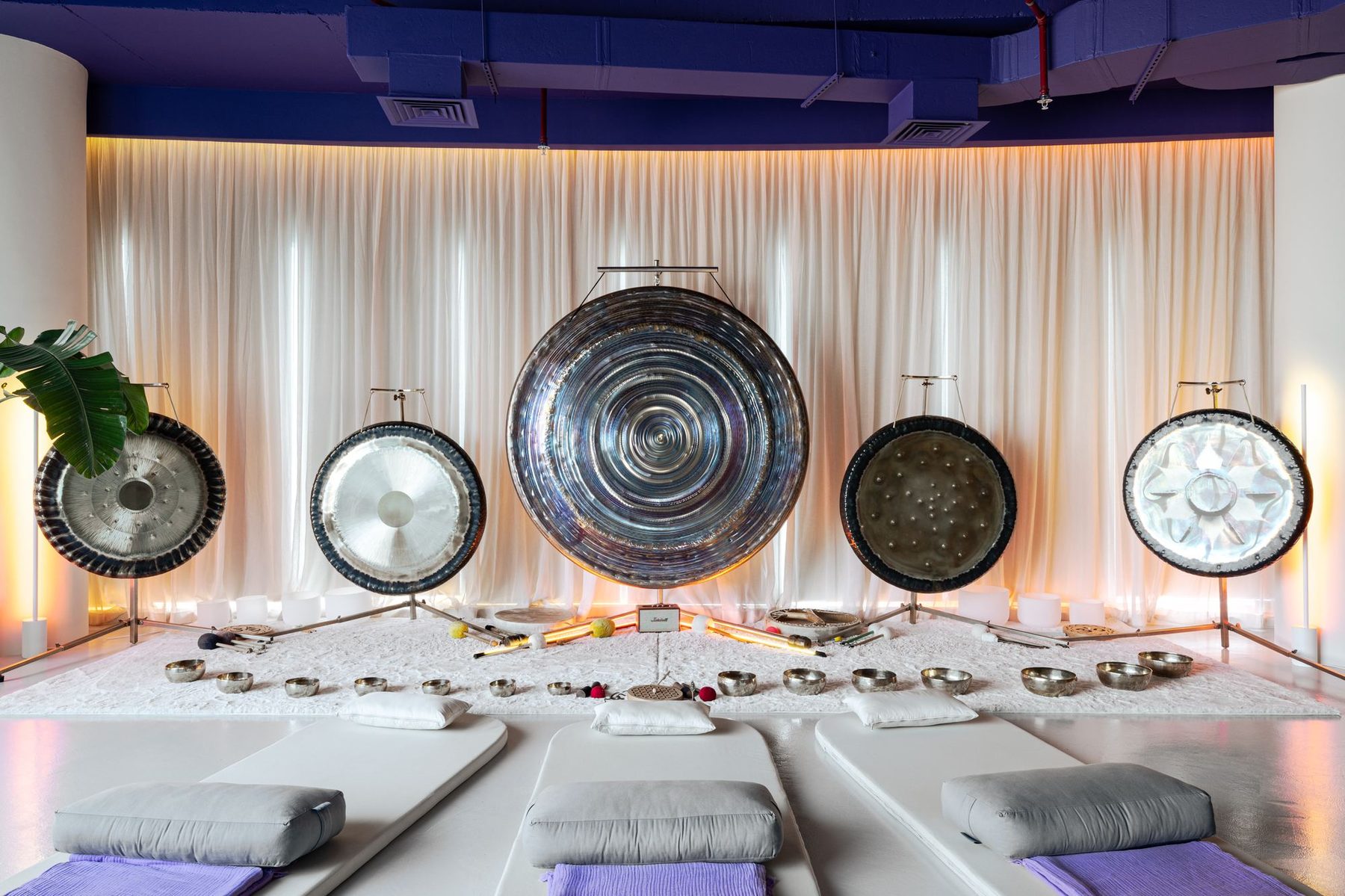 Gong wall of the sound healing studio — five gongs against backlit curtains with meditation mats