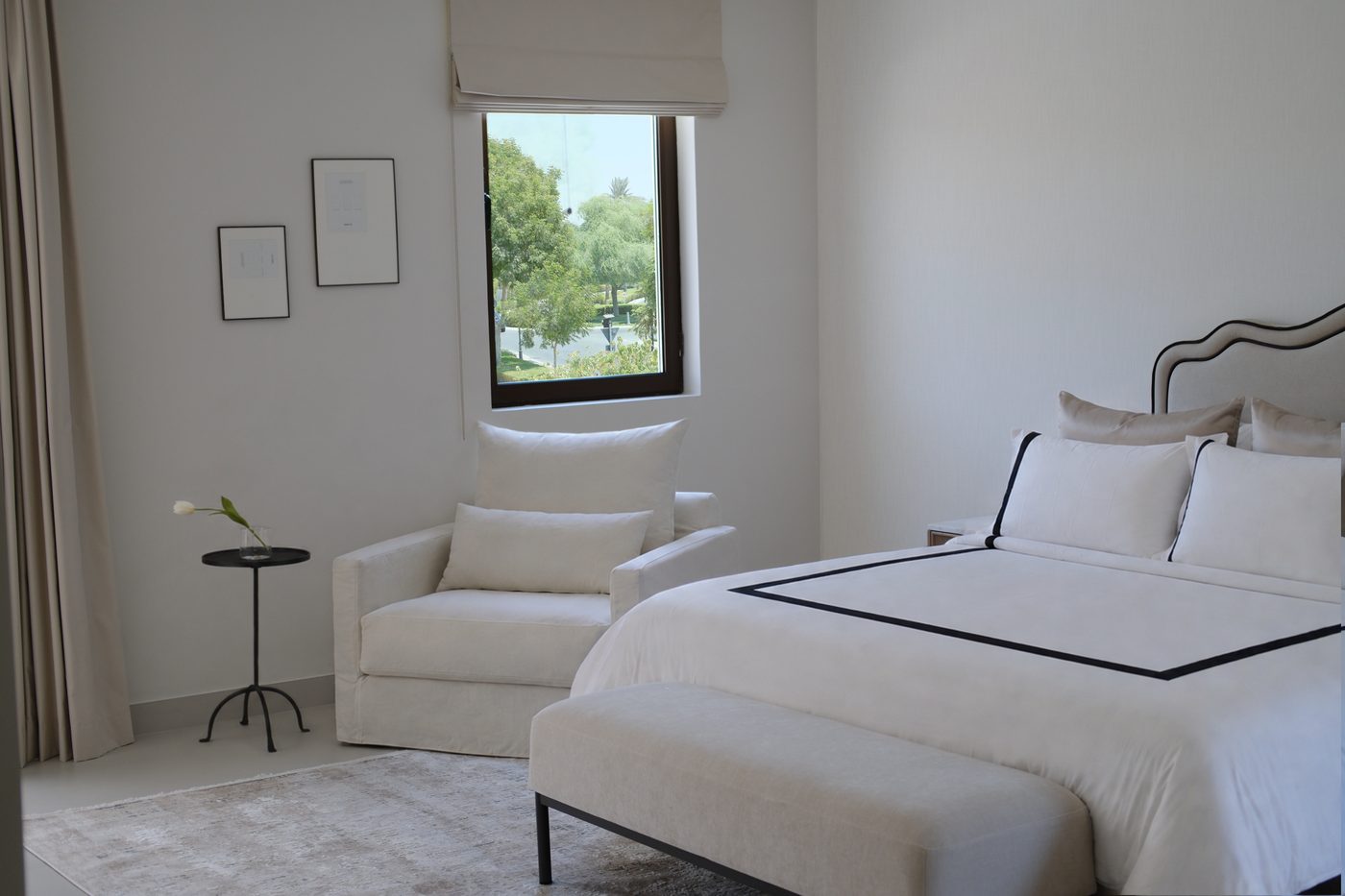 Master bedroom — white bedding with black trim, wavy headboard and armchair by the window