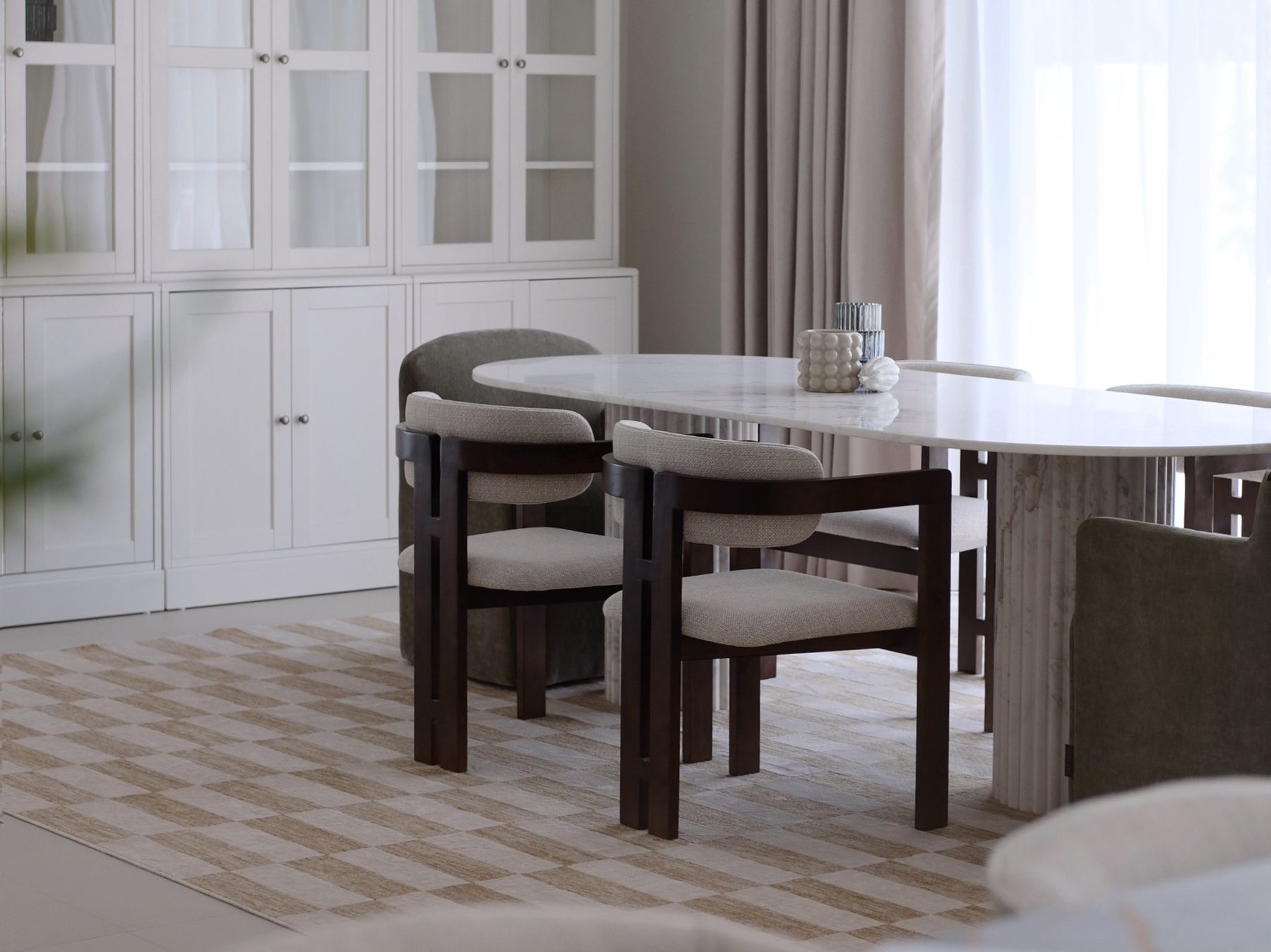 Dining room with oval marble table on fluted base and white glass-front cabinets