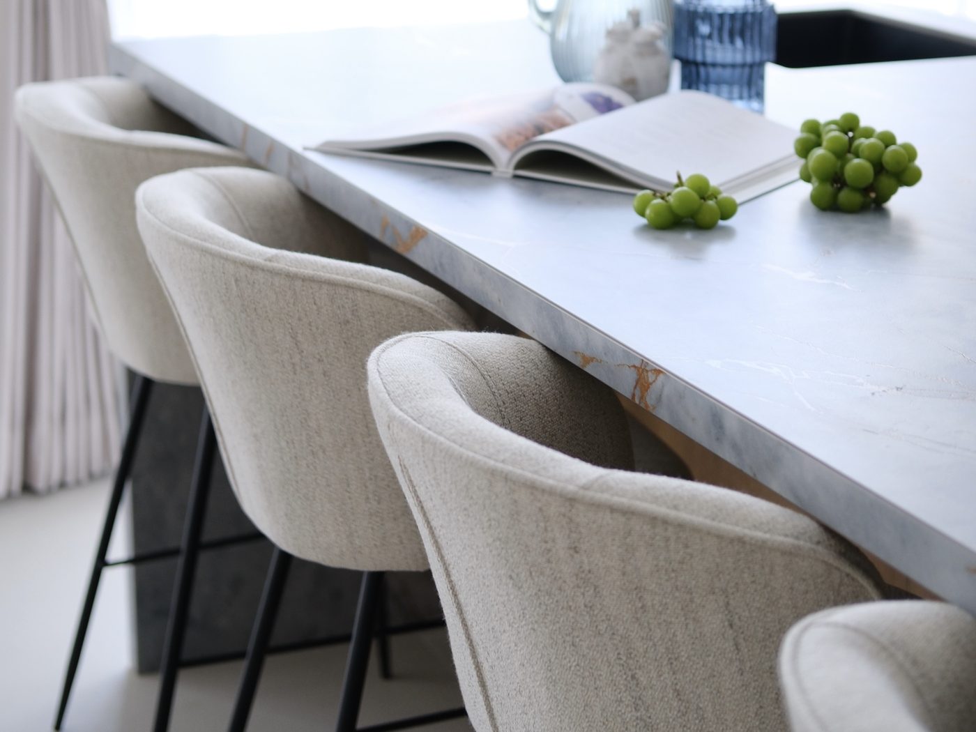 Kitchen island in storm-grey quartz with copper veining, boucle counter stools and green grapes