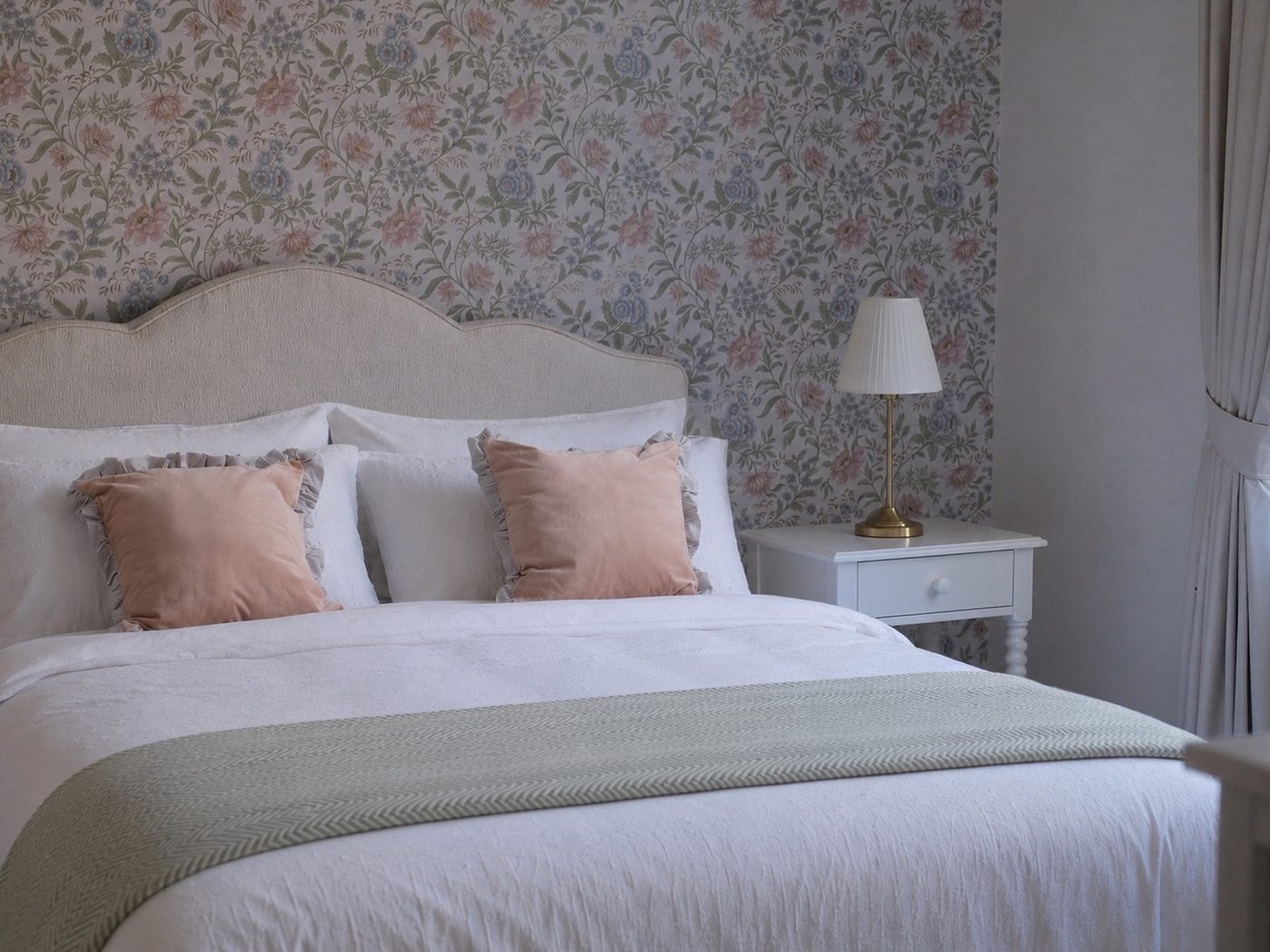 Girl's bedroom with floral wallpaper, cream headboard and blush velvet cushions