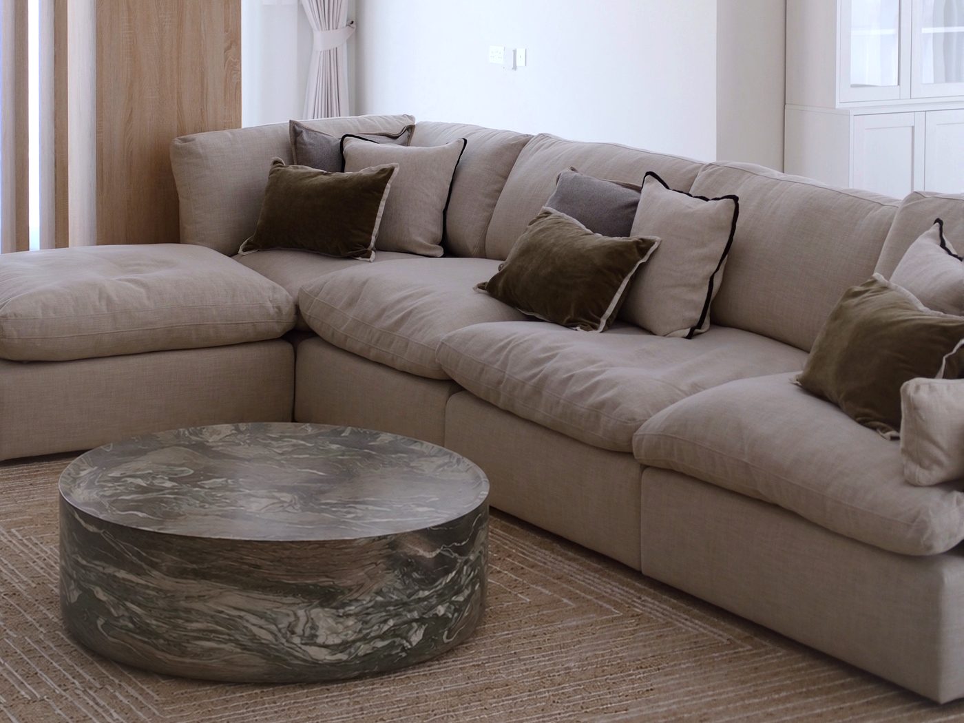 Living room — beige linen sectional sofa with olive velvet cushions and round marble coffee table